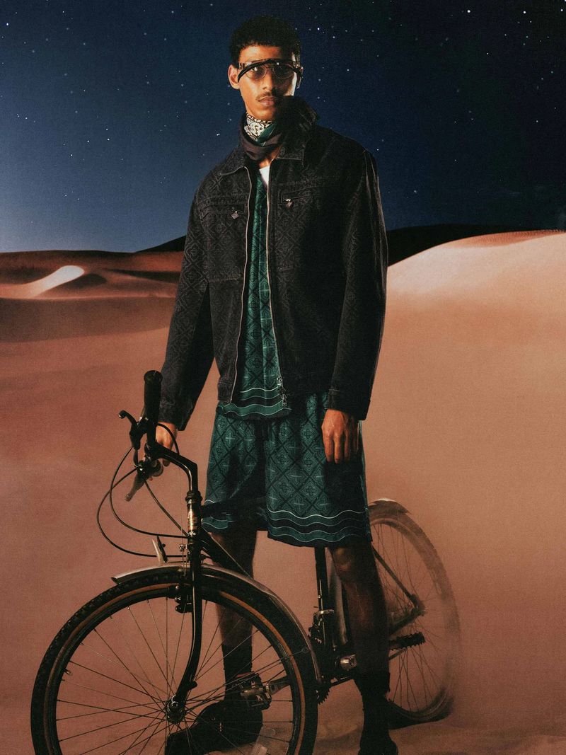 Model Mohamed Hassan standing with a bicycle in front of sand dunes under a starry night sky for Casablanca