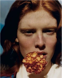 Close-up portrait of a woman with red hair holding a flower in her mouth for Twin Magazine.