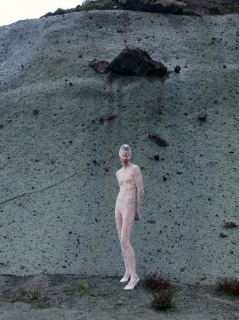 Model wearing patterned lace bodysuit standing in front of a textured stone cliff face