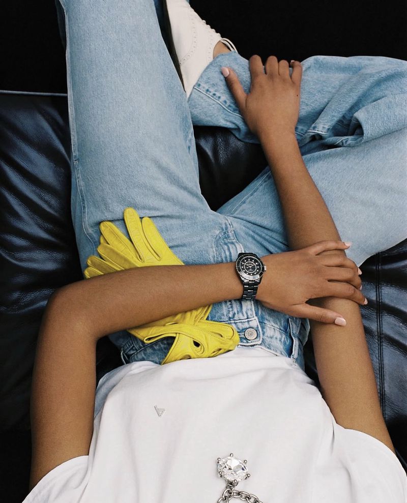Person seated wearing light blue jeans, white t-shirt, and holding bright yellow gloves against a dark leather seat