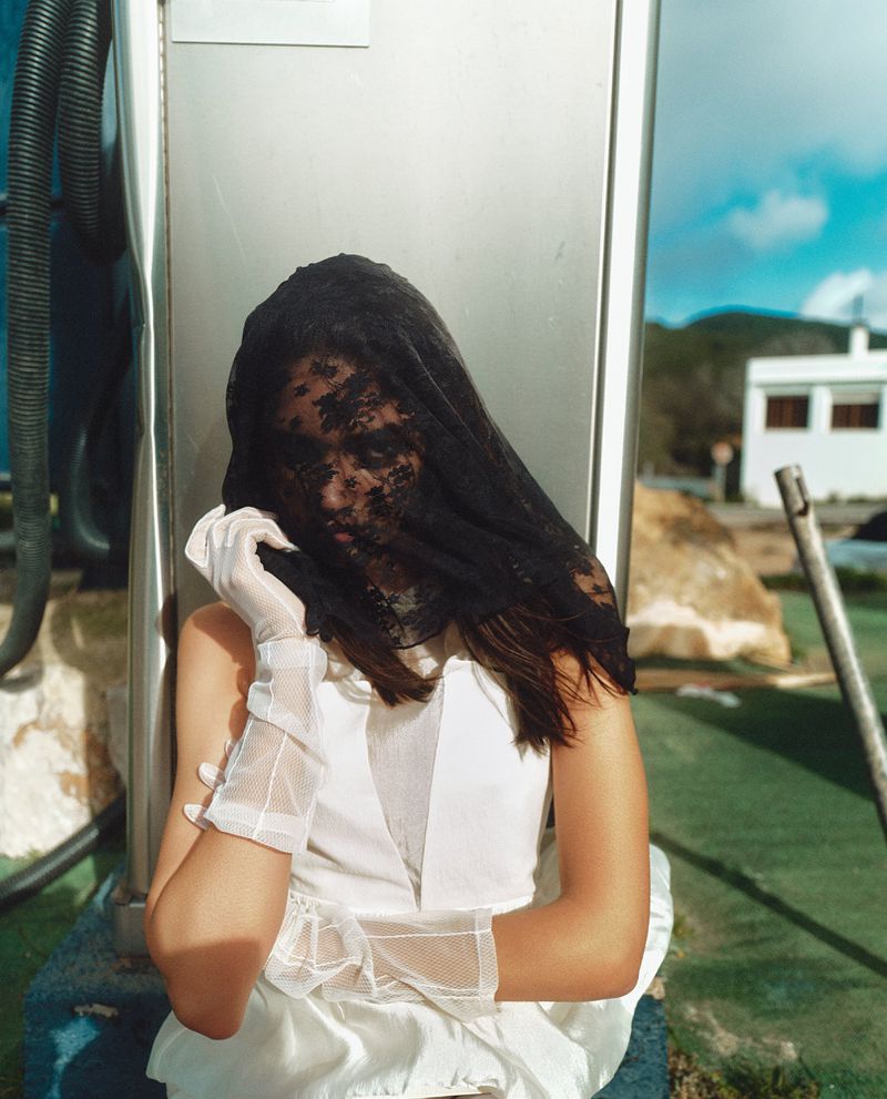 Model in white dress wearing a black lace veil and white gloves outdoors