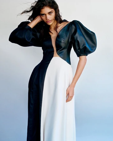 Model in a black and white dress with voluminous puff sleeves standing against a clean white backdrop