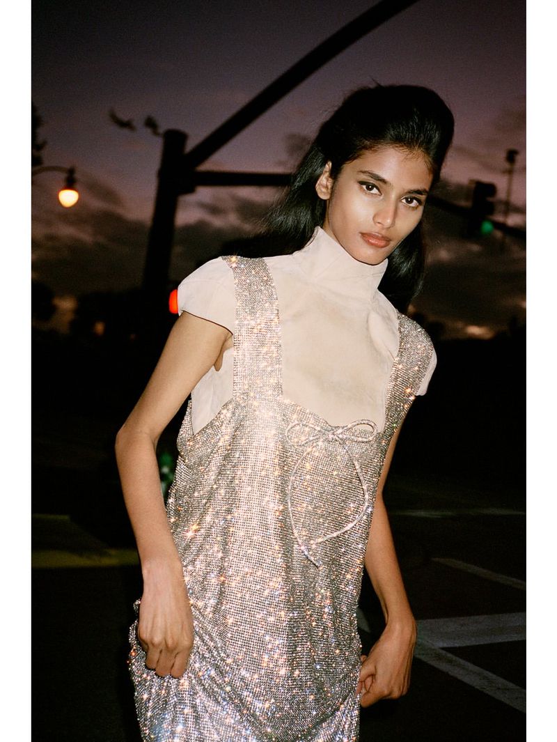 Model Bhavitha Mandava in a sparkling crystal-embellished dress standing outdoors at dusk for D Repubblica fashion editorial.