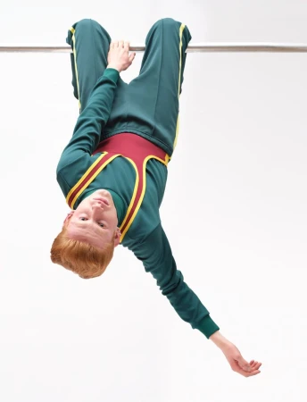 Model hanging upside down from a horizontal bar wearing a green tracksuit with red and yellow straps against white