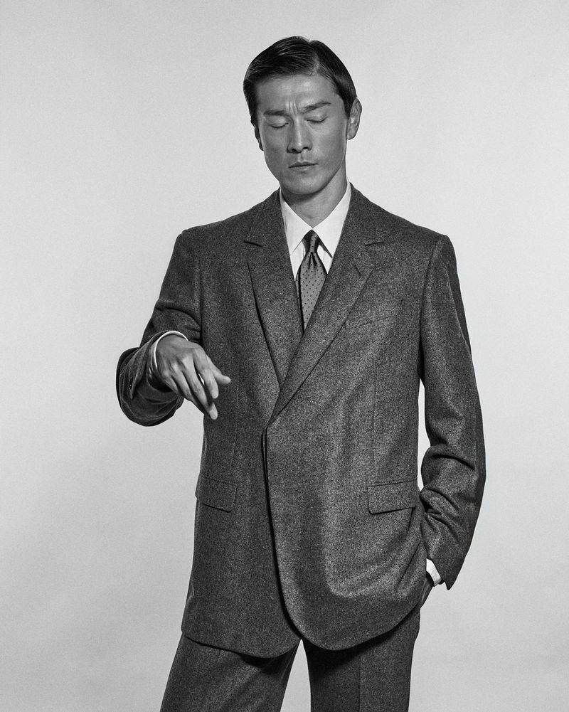 Model Daisuke Ueda wearing a grey tailored suit and tie for Corneliani, photographed by Simone Battistoni in monochrome.