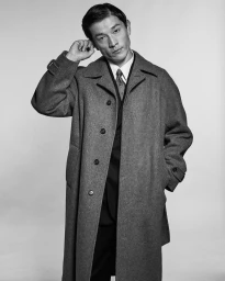 Monochrome portrait of a male model wearing a wool coat and tie with hand raised against a light studio backdrop.
