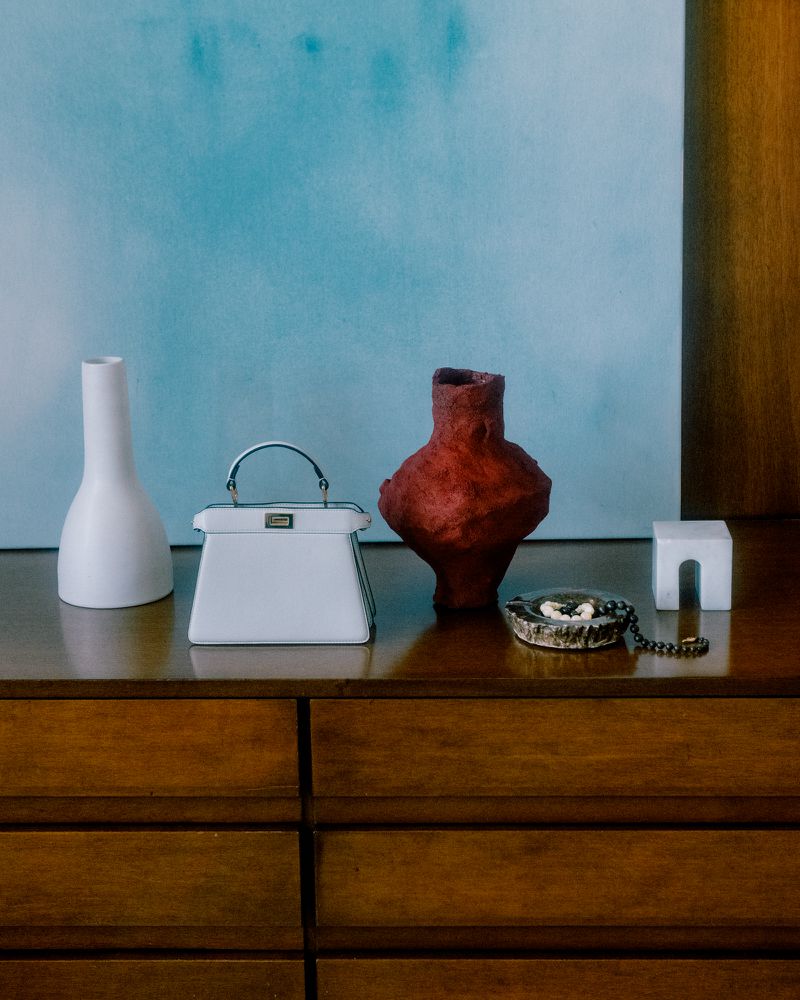 White handbag and textured red vase displayed on a wooden credenza against a blue panel for Z Magazine