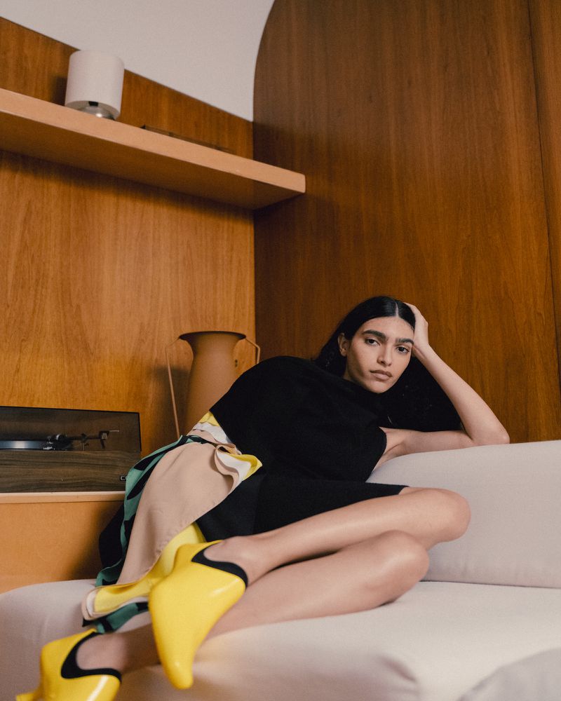 Model wearing yellow boots reclining on a white sofa in a wood-paneled room for Z Magazine Mode in Form editorial