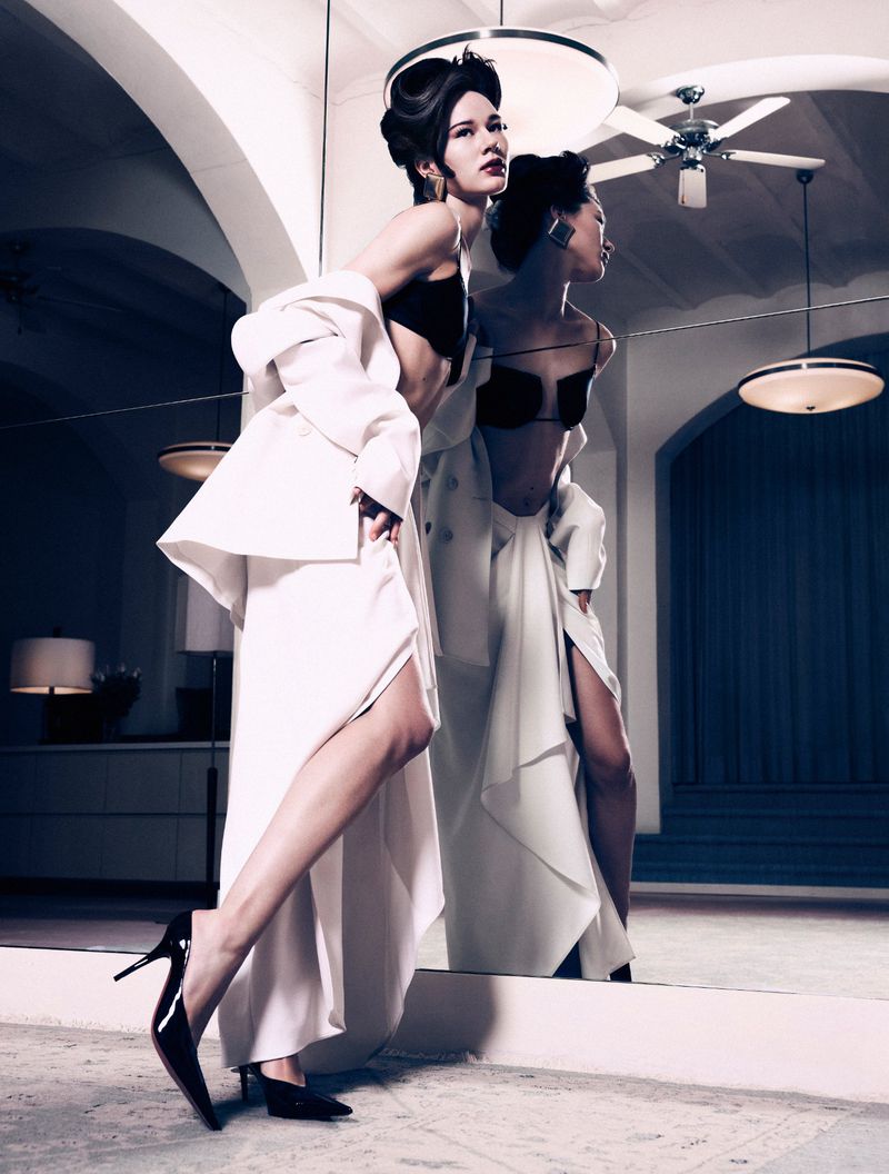 Model Lydia Celesta wearing a white suit jacket and skirt with black high heels posing in a mirror reflection for Numero Netherlands