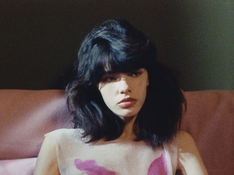 Portrait of a woman with dark hair and fringe seated against a muted pink background for Luncheon Magazine SS26.
