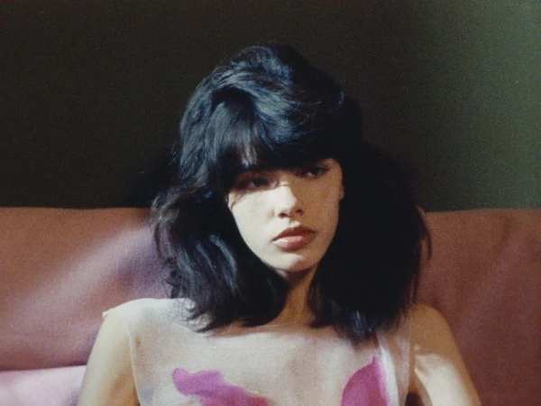 Portrait of a woman with dark hair and fringe seated against a muted pink background for Luncheon Magazine SS26.
