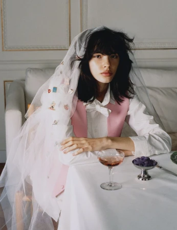 Model wearing a pink vest and sheer white veil seated at a table with a cocktail glass for Luncheon Magazine SS26.