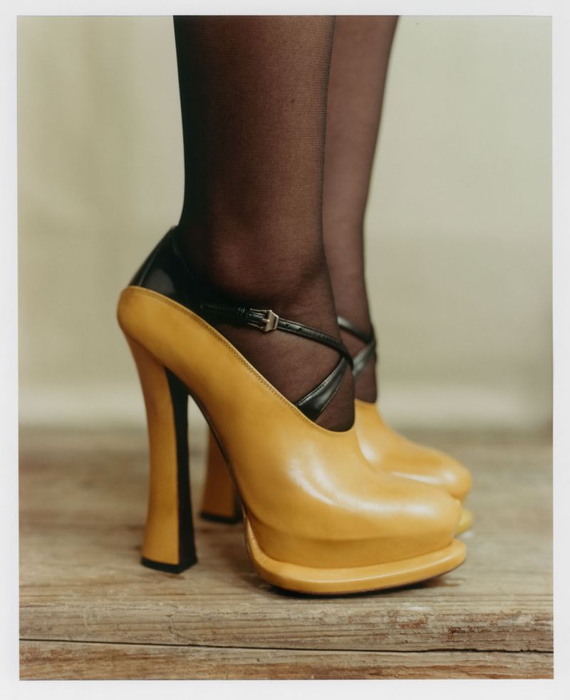 Close-up of legs in black tights wearing thick-heeled tan platform shoes on wooden flooring