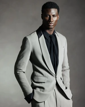 Black man wearing a grey suit jacket and black shirt against a neutral grey studio backdrop