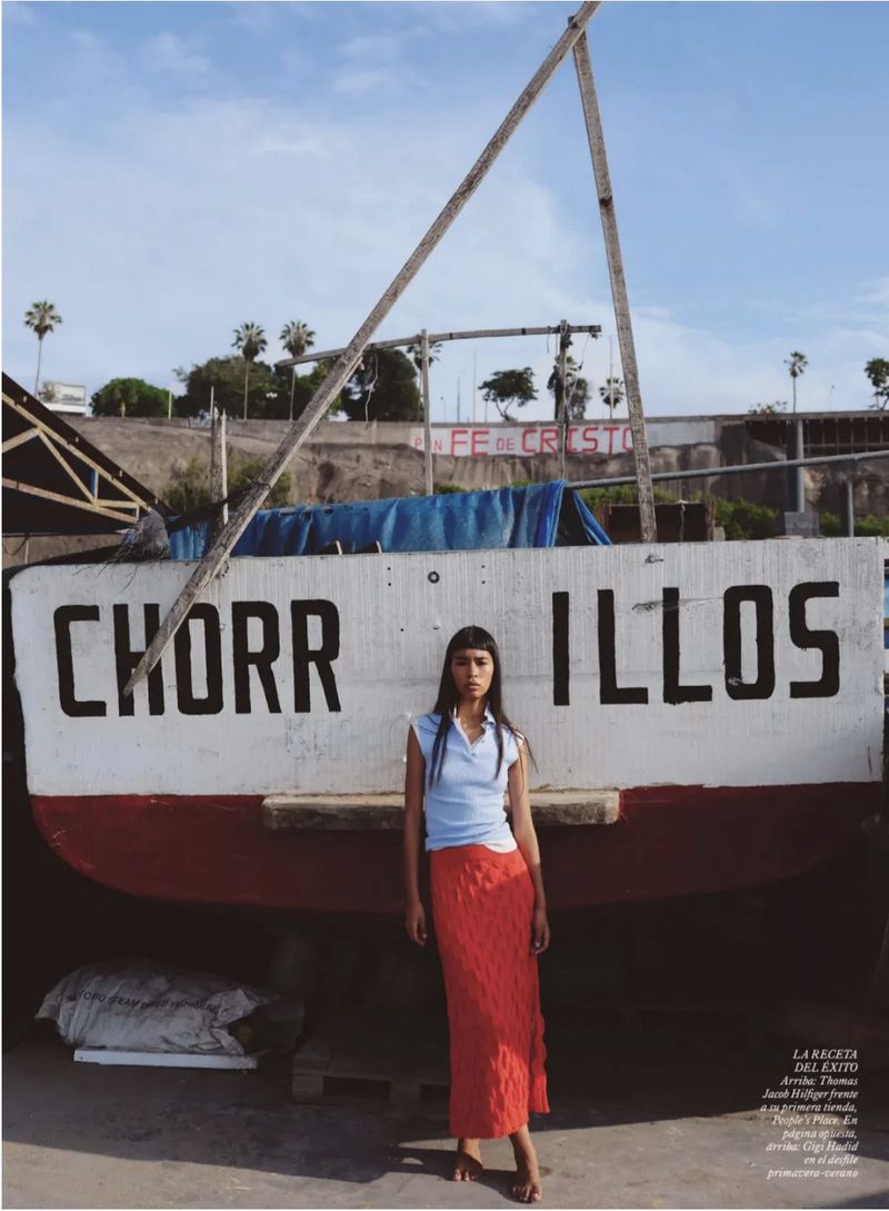 Model standing in front of a large painted fishing boat labeled Chorrillos with a blue sky background.