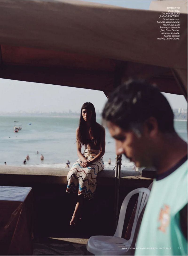 Woman sitting on a wall overlooking the ocean while a man in a teal shirt is out of focus in the foreground.