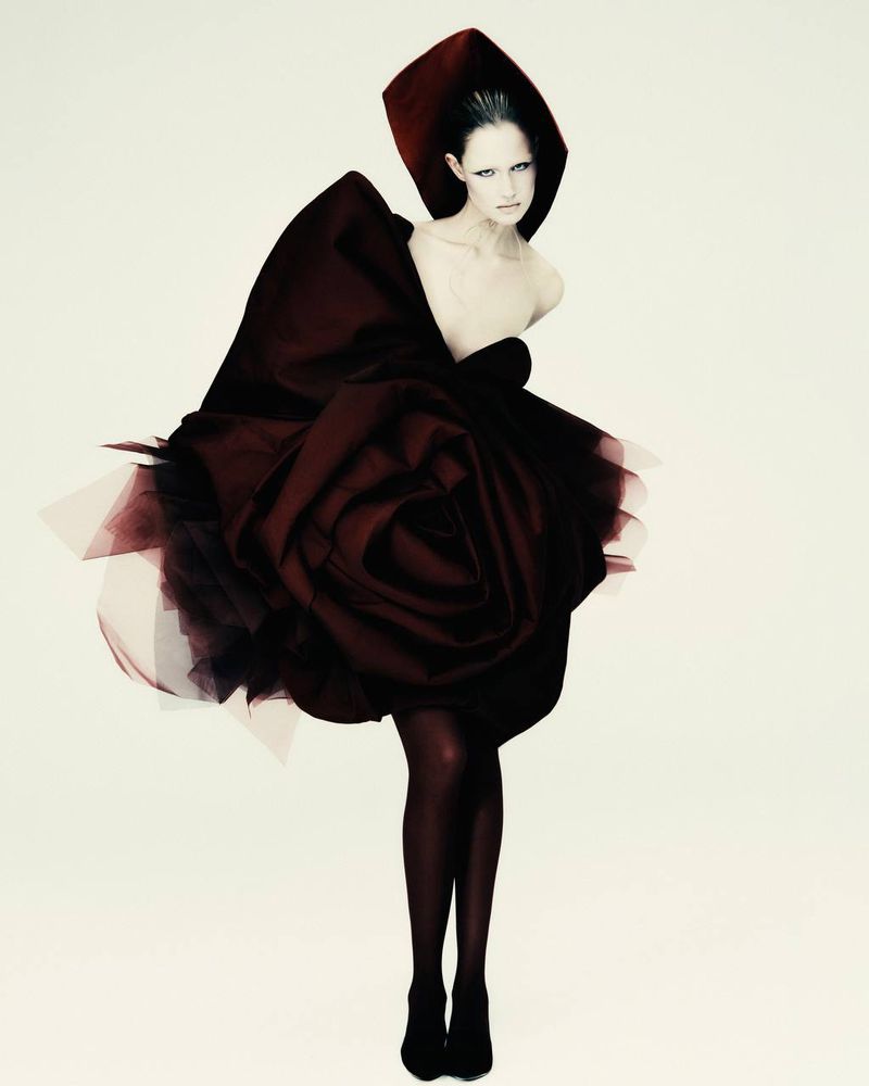 Fashion photo of a single woman in a couture gown, featuring a large rose-like skirt and matching head covering against a white background.