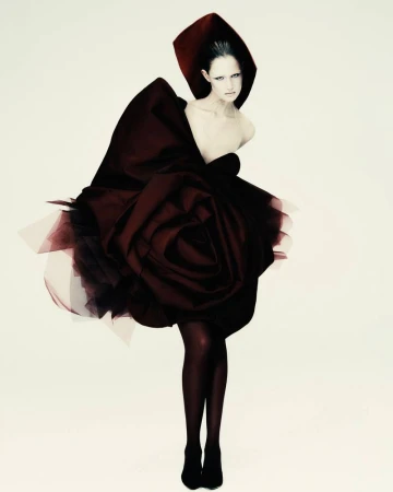 Fashion photo of a single woman in a couture gown, featuring a large rose-like skirt and matching head covering against a white background.