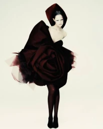 Model in architectural burgundy rose-shaped sculptural dress against a white studio background