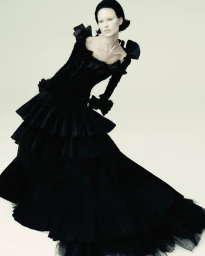 Model in a dramatic black tiered gown posing against a plain white background for Vogue Adria Couture Bloom.