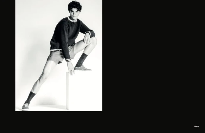 Model crouching on white pedestal wearing dark knit sweater and shorts for Numéro Homem Brasil editorial
