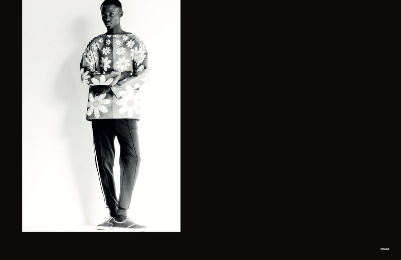 Black and white fashion portrait of a male model wearing a patterned floral long-sleeve top and trousers against a light backdrop.