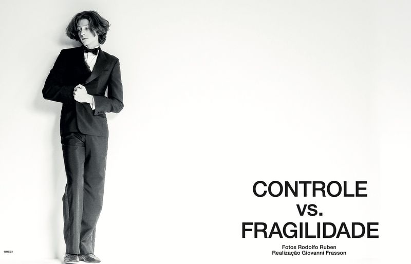 Monochrome fashion editorial image of a male model wearing a black tuxedo and bow tie against a bright white background.