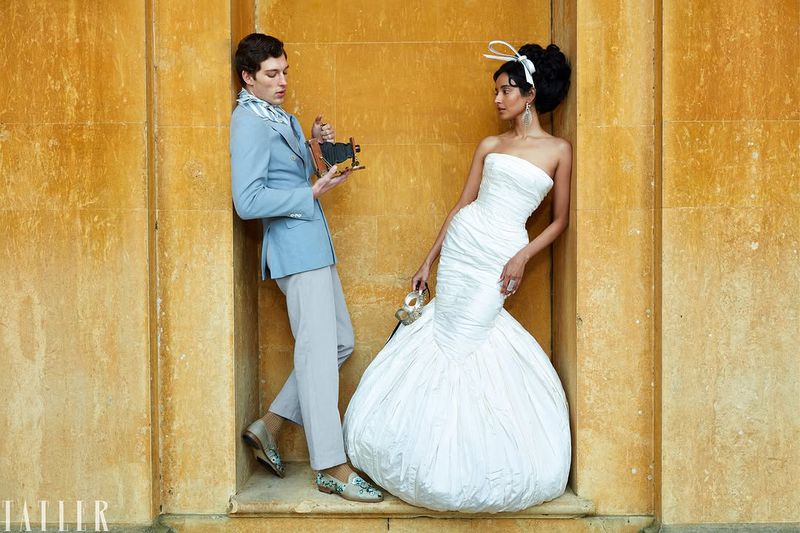 Man holding a vintage camera and woman in a white ballgown posing inside architectural stone wall niches for Tatler U.K.