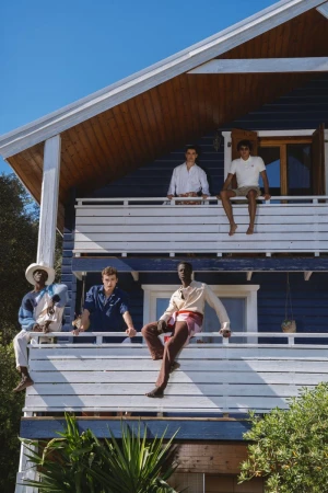 Four male models posing on the balconies of a blue wooden house under a clear sky.