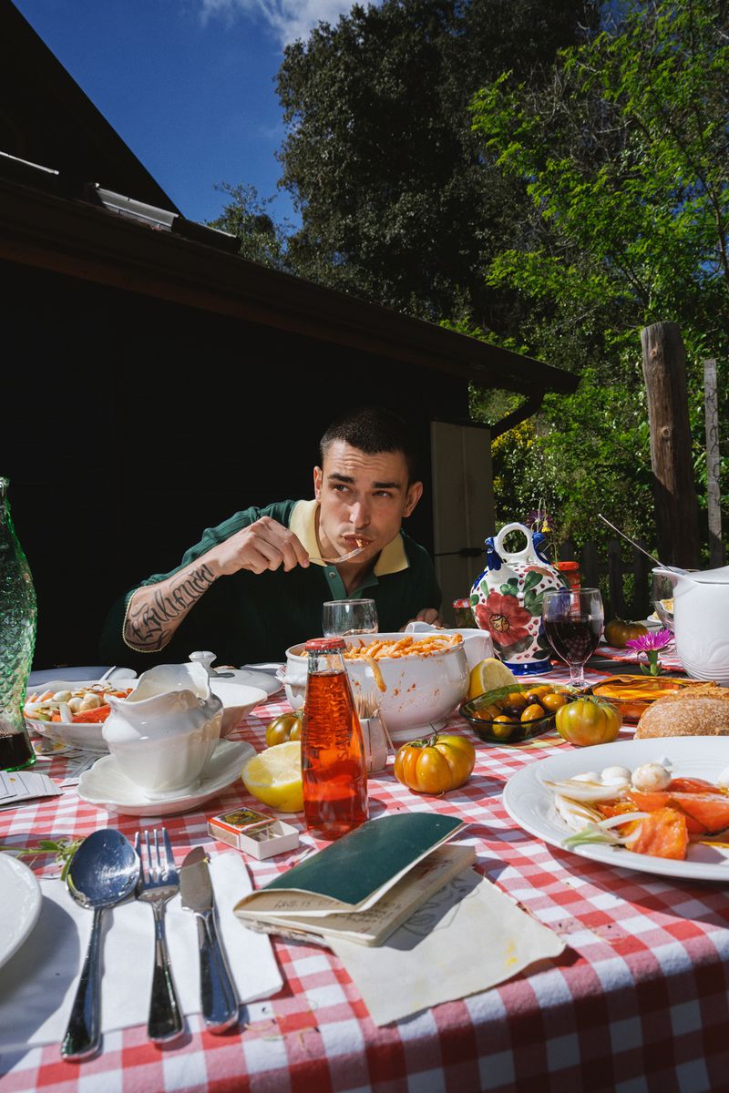 Man eating food at an outdoor picnic table with a red checkered tablecloth under trees