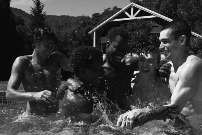 Black and white photograph of five young men laughing and splashing water in an outdoor pool, captured by Vinyet Feliubadaló.