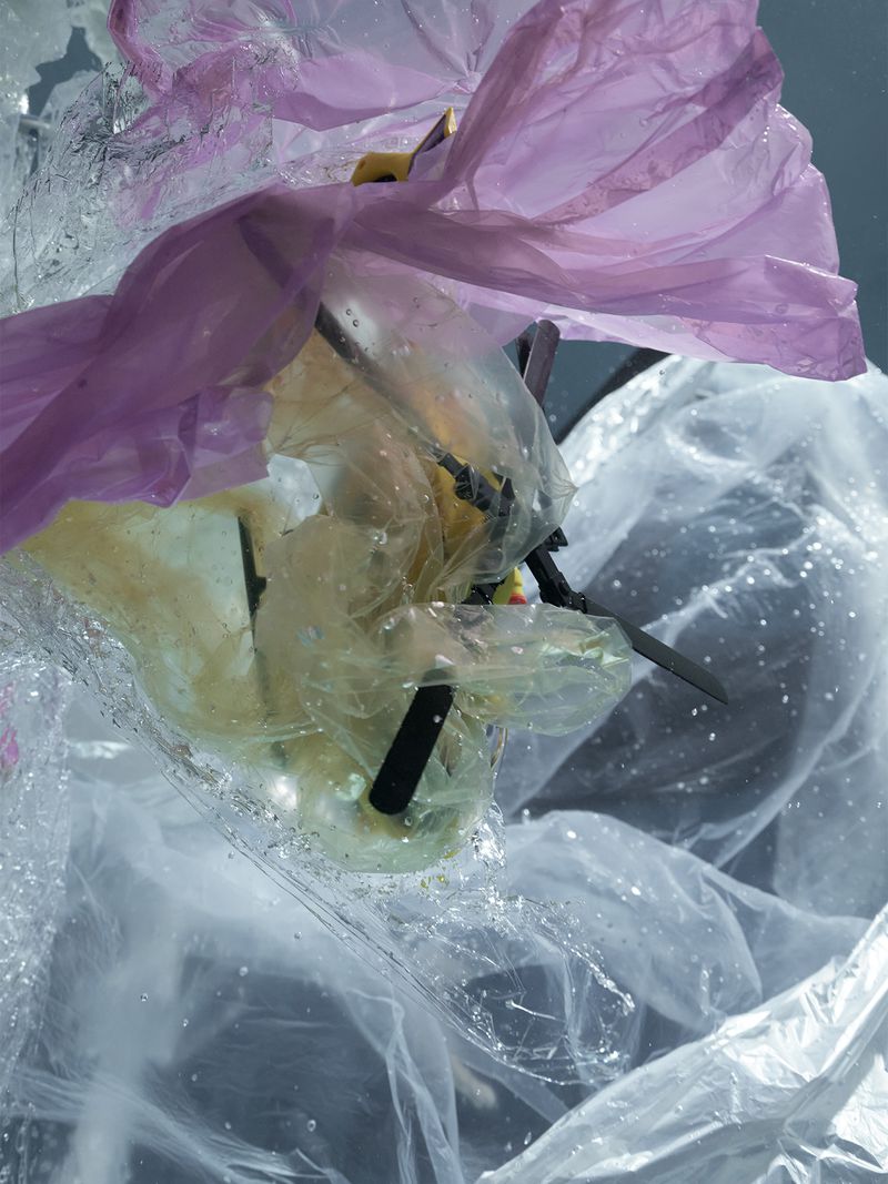 Toy helicopter wrapped in crinkled clear and purple plastic wrap underwater with scattered air bubbles