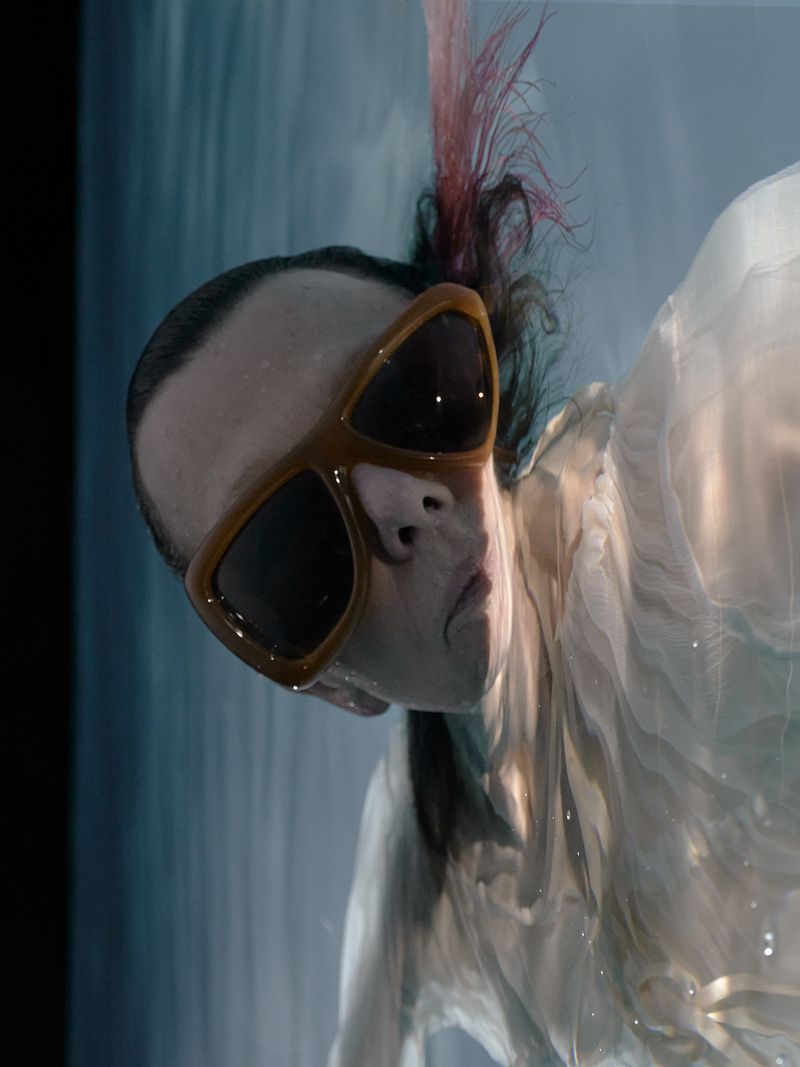 Florentina Holzinger wearing large brown sunglasses and a white dress underwater for Re-Edition Magazine