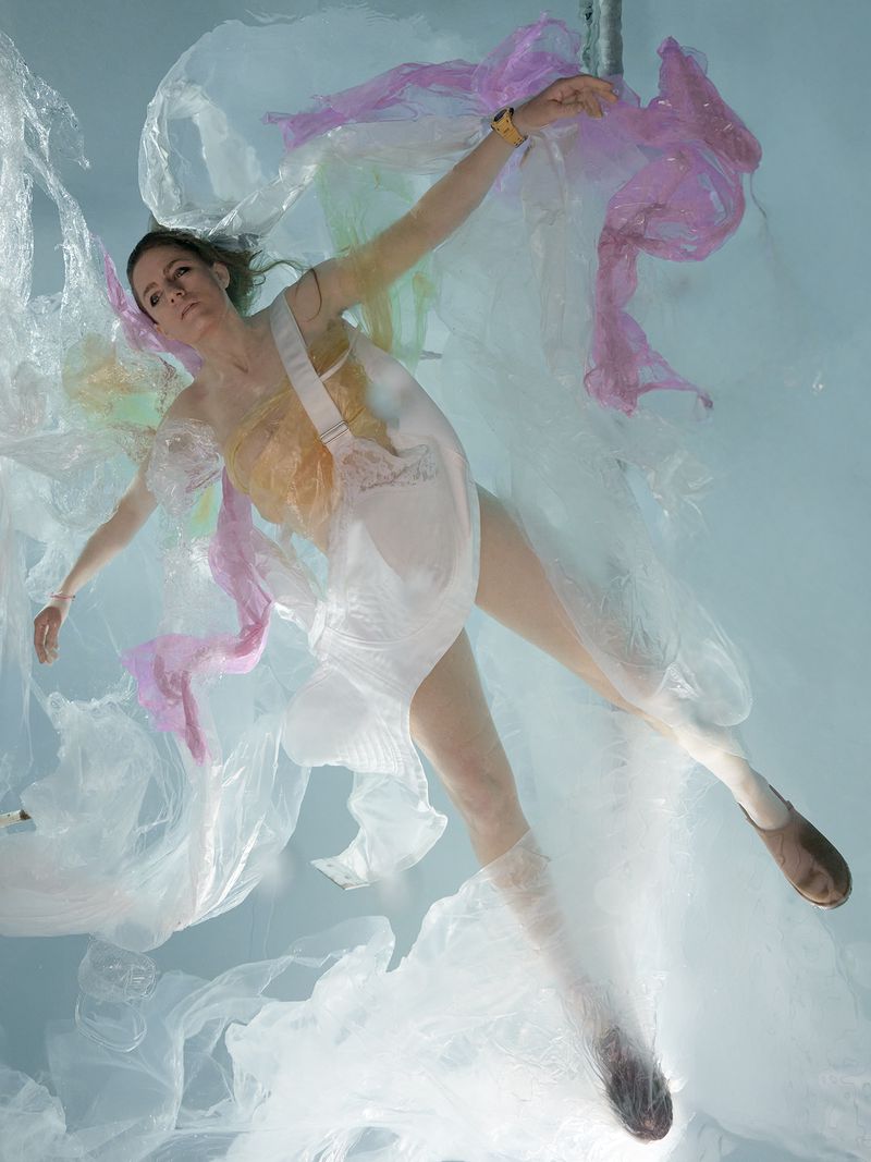 Woman floating underwater surrounded by flowing translucent plastic sheets in pink and yellow for Re-Edition Magazine
