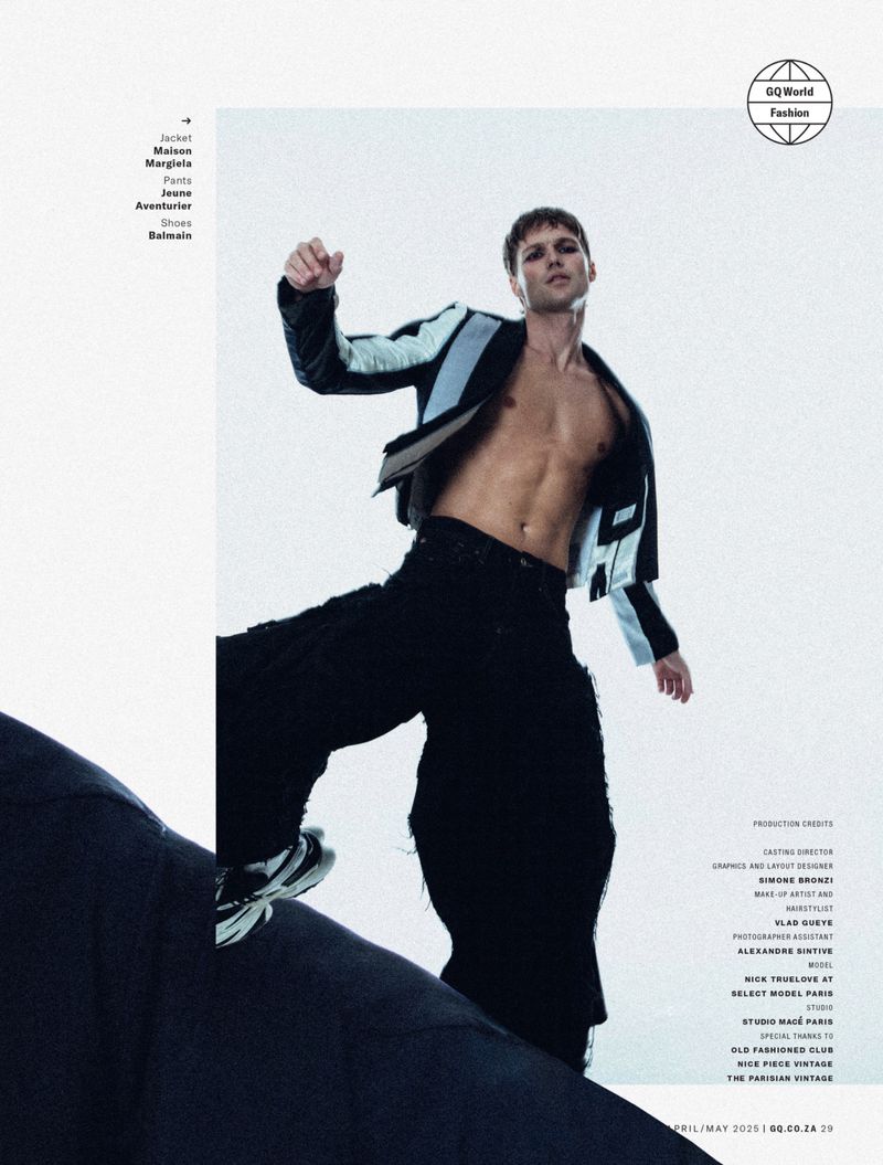 Model Nick Truelove posing shirtless in a black and blue jacket and black pants against a white background for GQ South Africa.