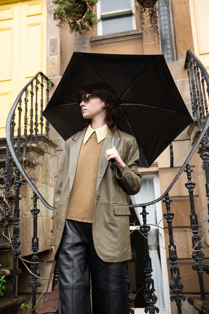Woman holding a black umbrella standing on an outdoor staircase in front of a building exterior with wrought-iron railings.