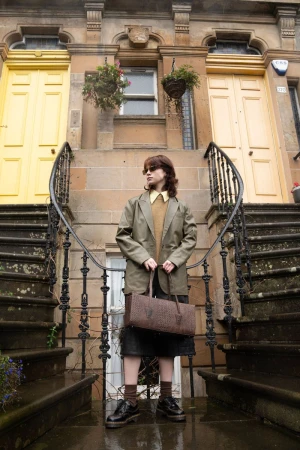A woman standing on stone steps holding a rectangular leather handbag in front of two yellow doors