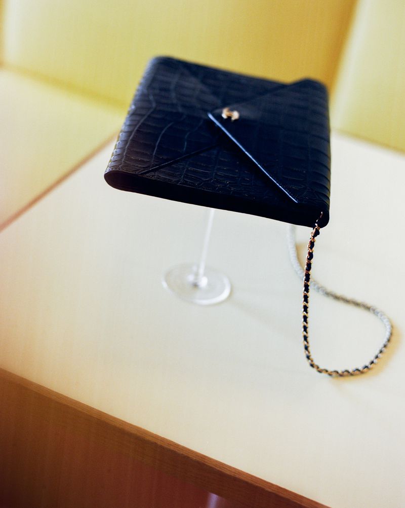 Black leather quilted envelope handbag on a clear stand against a soft yellow background