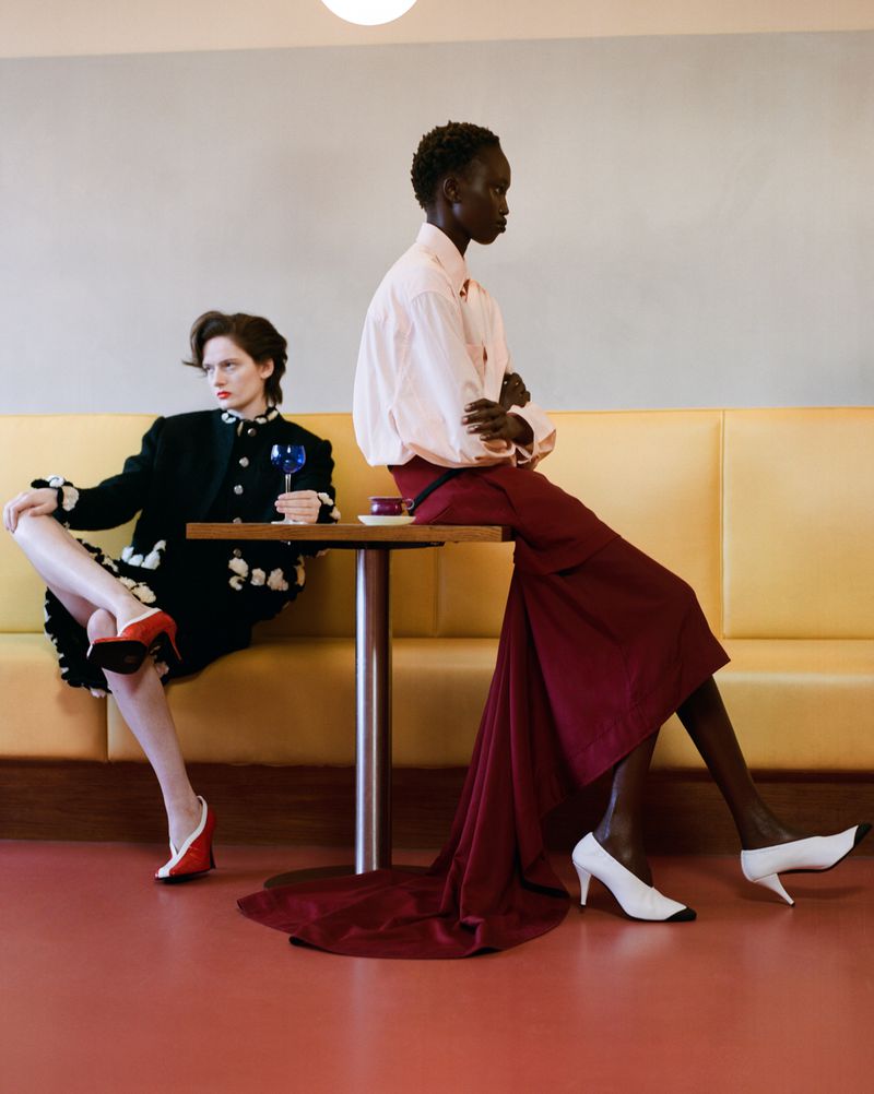 Two female models seated at a cafe table against a yellow booth and red floor for Vogue Czechoslovakia