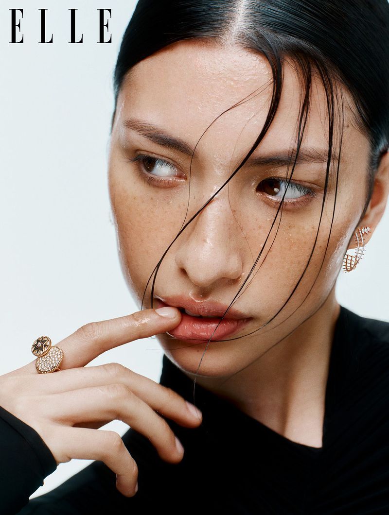 Close-up beauty portrait of a model with wet hair touching lips wearing rings and earrings against a white background for Elle UK.