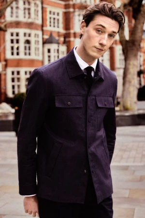 Model Harvey James in a dark navy jacket and tie standing outdoors for Carolina Herrera Matryoshka Pocket Campaign