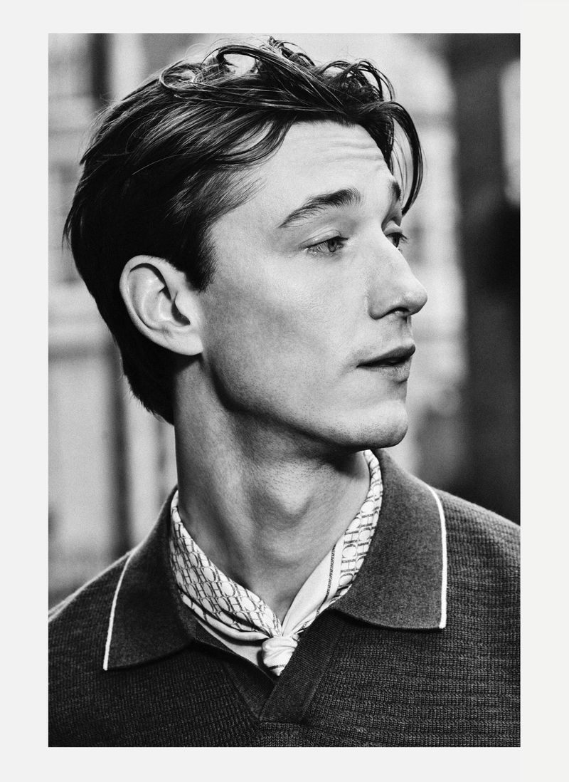 Black and white portrait of a man wearing a patterned neck scarf and polo shirt for Carolina Herrera