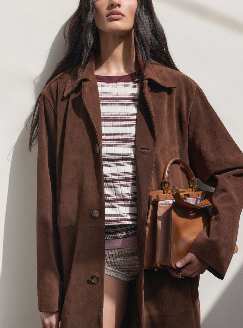 Model wearing a brown suede coat and holding a leather handbag for Harper's Bazaar UK editorial