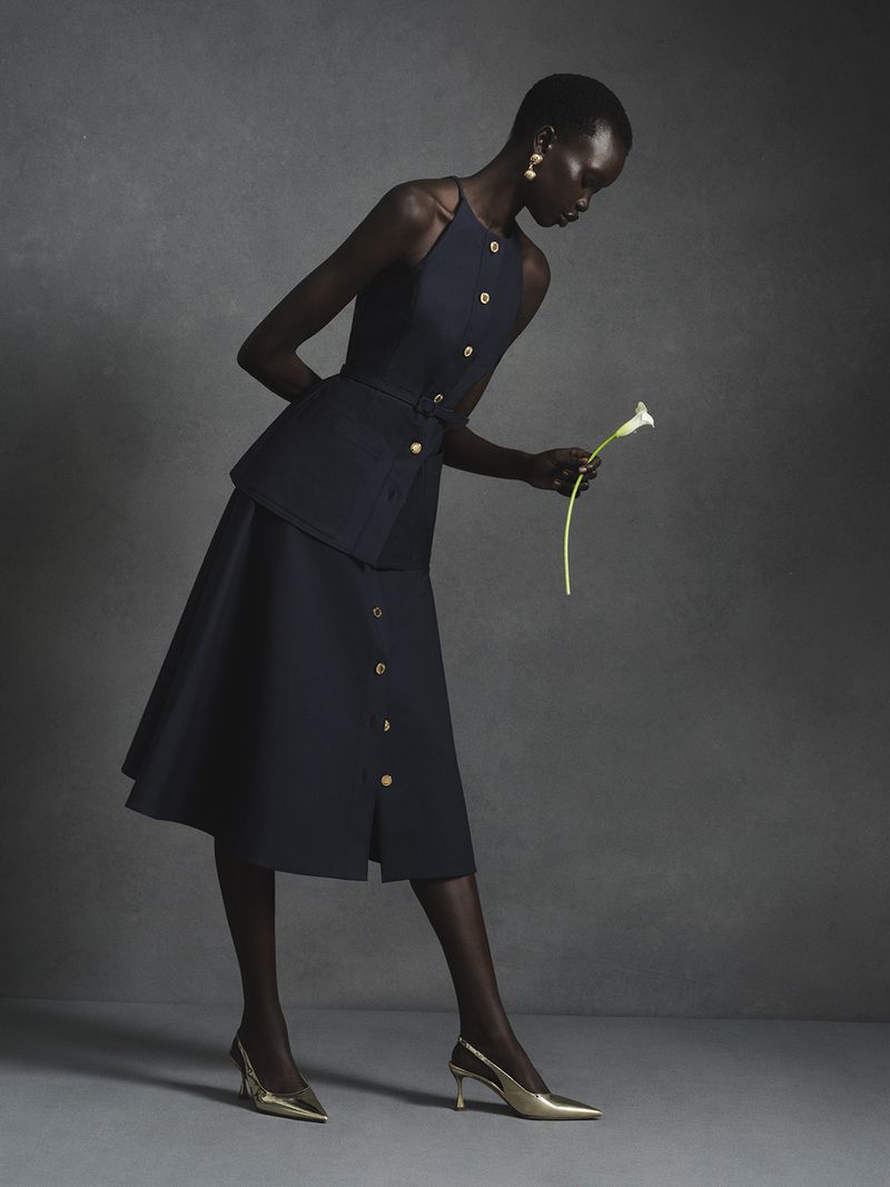 Model in navy halter top and matching skirt holding a white calla lily against a grey textured studio backdrop
