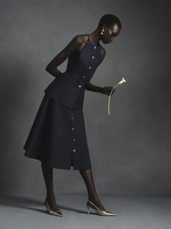 Model in navy halter top and matching skirt holding a white calla lily against a grey textured studio backdrop