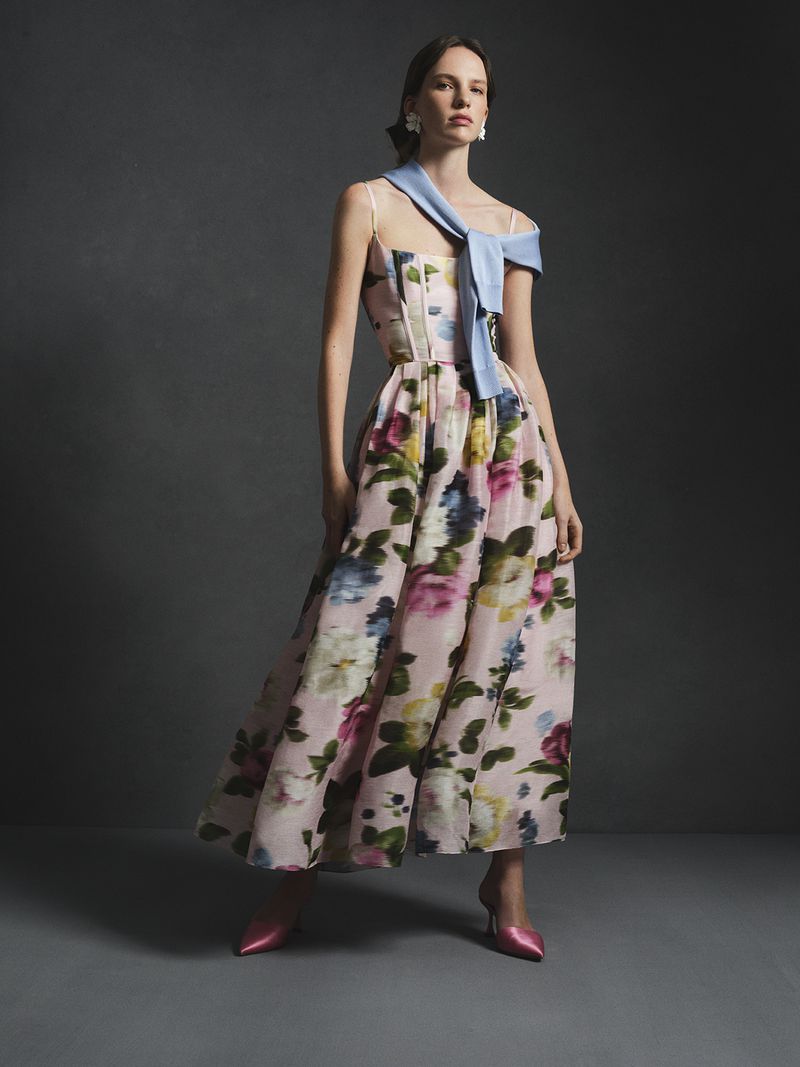 Model in a floral print midi dress with a light blue sweater tied over one shoulder against a dark studio background