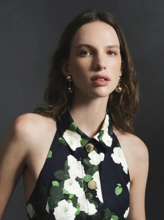 Model in a black floral halter dress with gold buttons posing against a grey studio backdrop