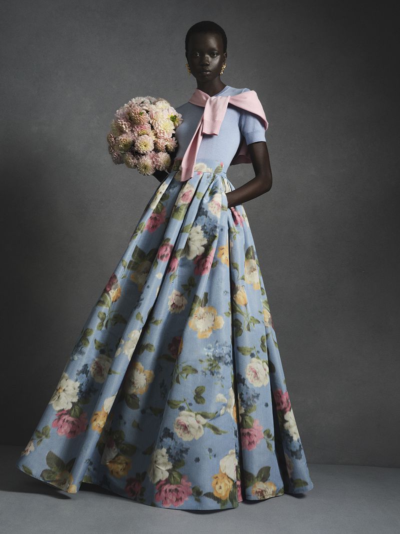 Model in a floral print ball gown holding a large bouquet of pink flowers for Carolina Herrera.