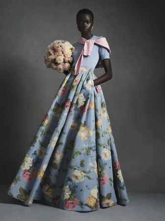 Model in a floral print ball gown holding a large bouquet of pink flowers for Carolina Herrera.