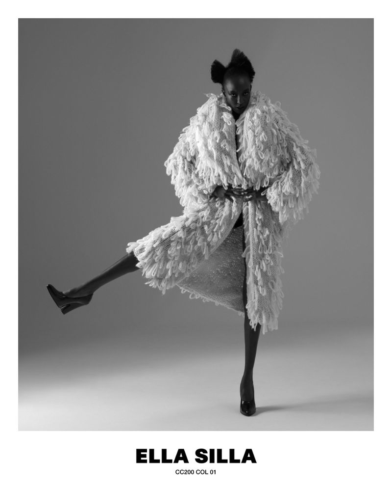 Model in textured white fluffy coat and heels posing against a grey studio backdrop for Ella Silla project.